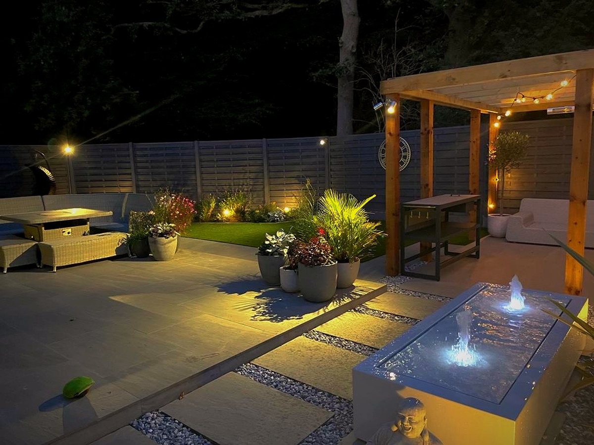 Outdoor pergola with festoon lights and water feature at night